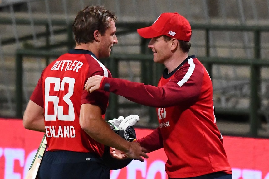 A cap-wearing English cricket captain shakes hands with his teammate after a T20I win.