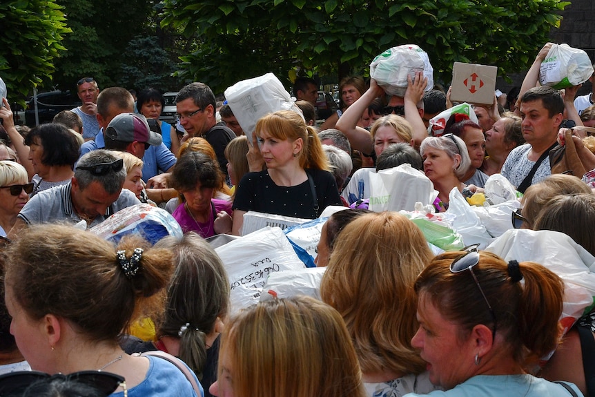 A dense crowd of people pass plastic shopping bags full on medicines and clothes.