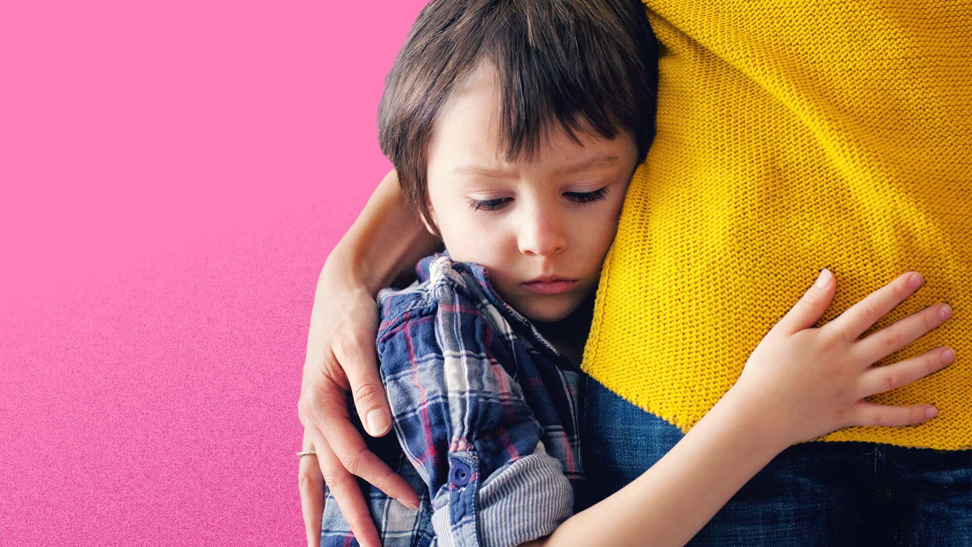 Young boy with dark hair and a blue check shirt hugs the hip of a woman wearing a yellow jumper and blue jeans