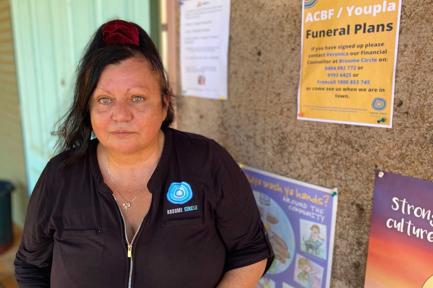 A woman sits in front of a noticeboard with posters.