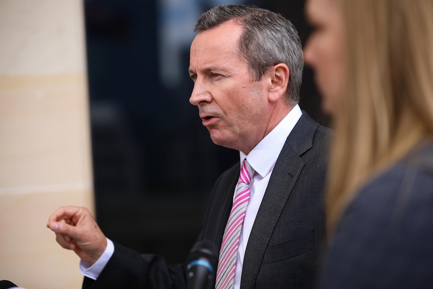 A close-up side-on shot of WA Premier Mark McGowan speaking outside state parliament, with a woman out of focus on his left.
