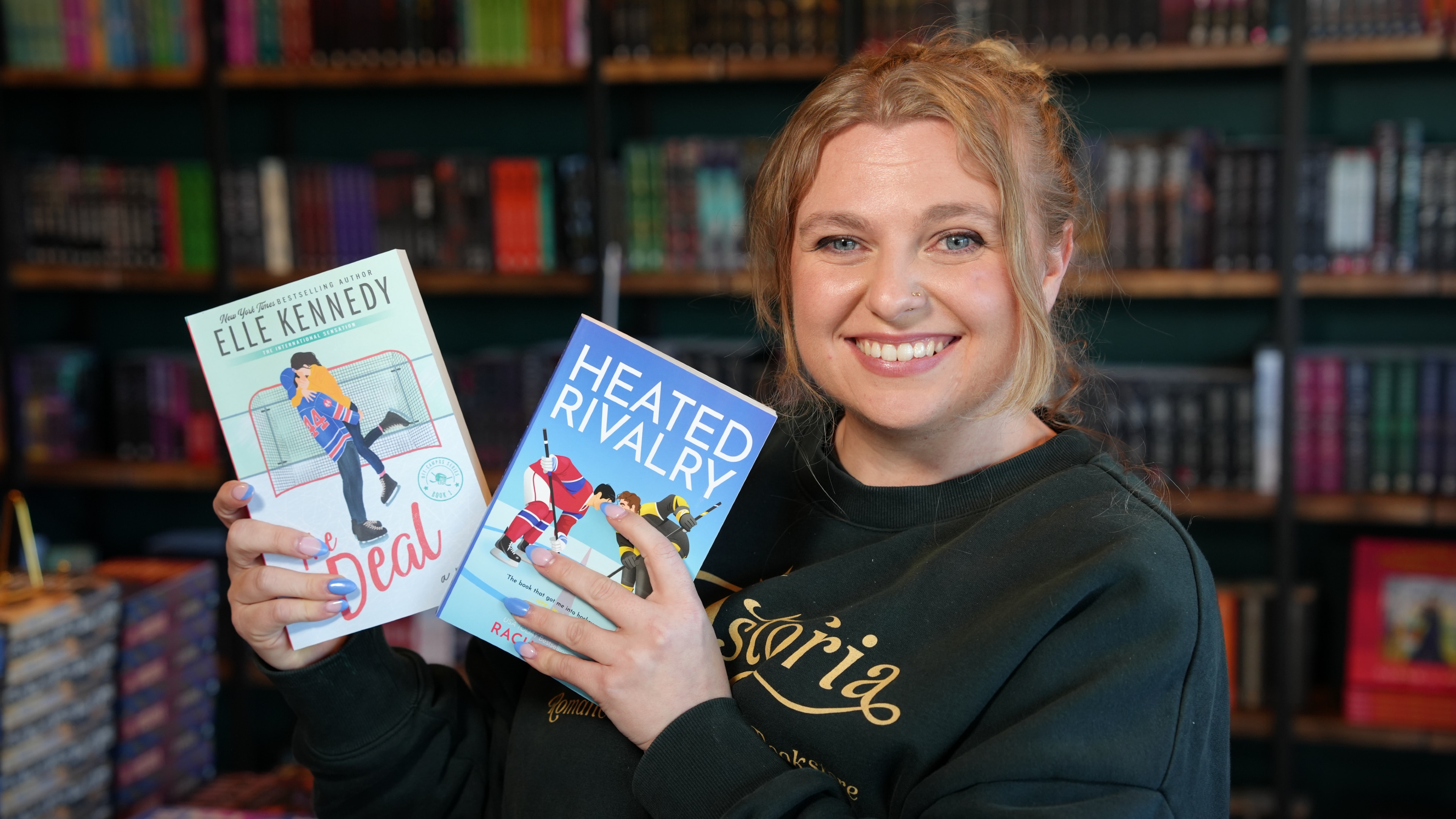 A woman smiles holding two books standing in a bookstore.