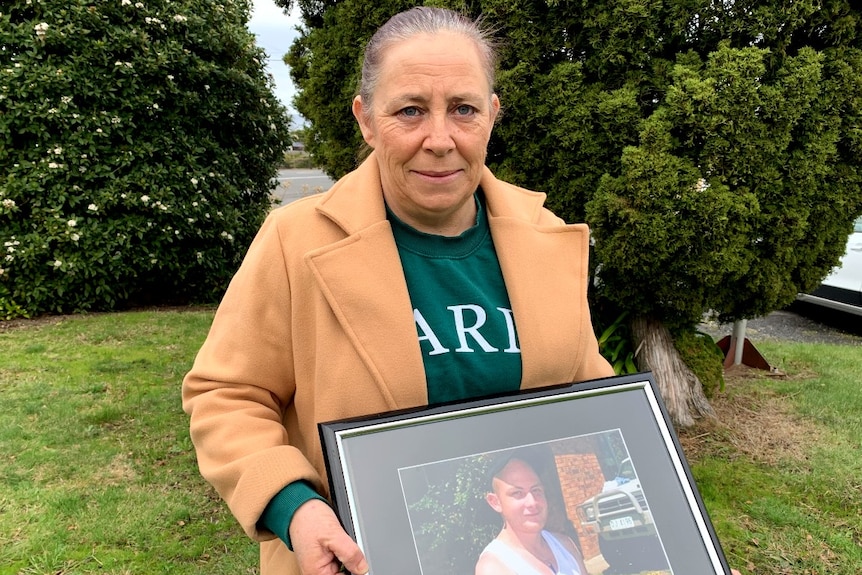 A middle aged woman holds a framed photo of her adult son