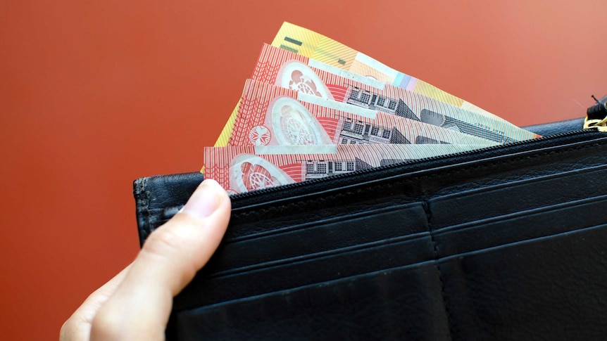 A woman holds a black wallet with three $20 notes and a $50 note, for a story on budgeting.