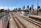 A train line stretches into the distance, the Perth skyline is visible.