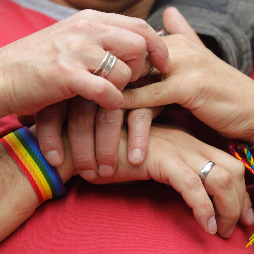 People hold hands with rainbow bracelets and rings.