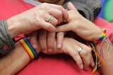 People hold hands with rainbow bracelets and rings.