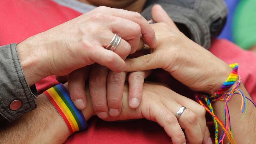 People hold hands with rainbow bracelets and rings.