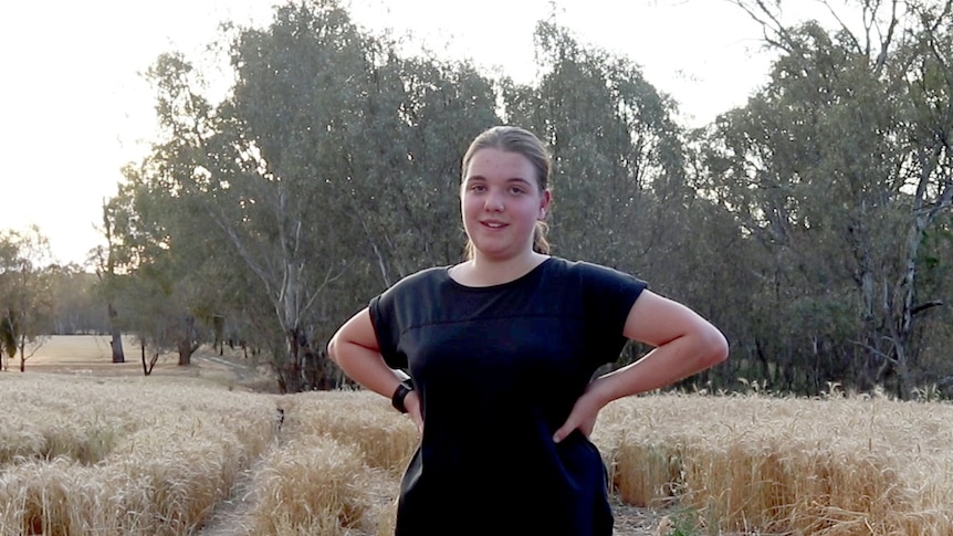 A teenage girl stands, with hands on hips, in a paddock after a run