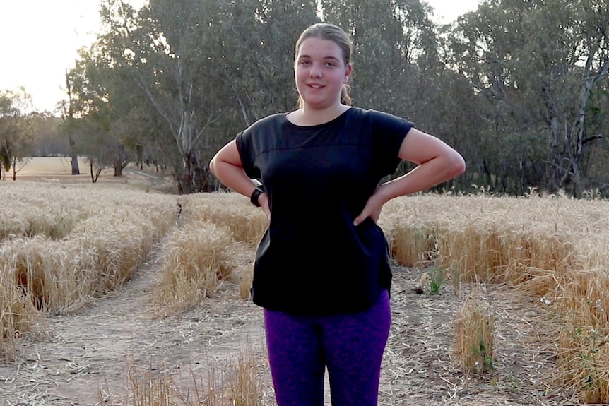 A teenage girl stands, with hands on hips, in a paddock after a run