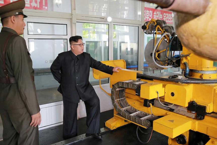 North Korean leader Kim Jong-un looks at a large yellow piece of equipment.