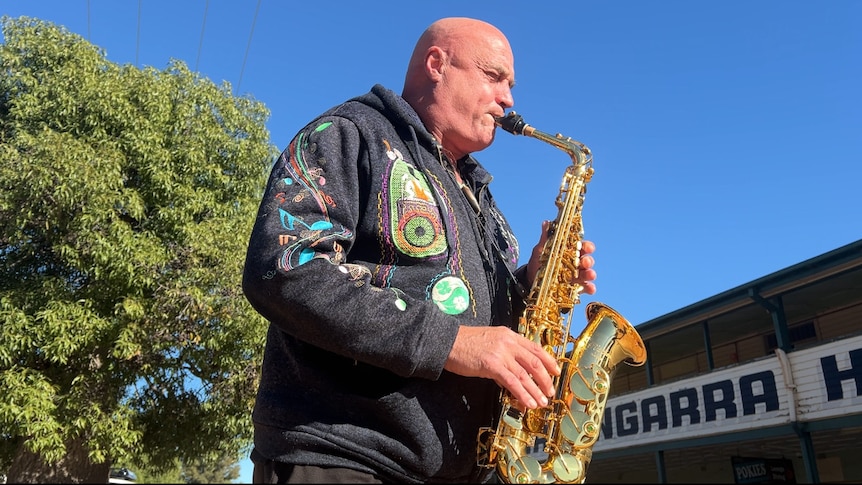 Man playing saxophone in the sun outside a pub. 