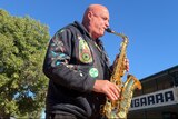 Man playing saxophone in the sun outside a pub. 