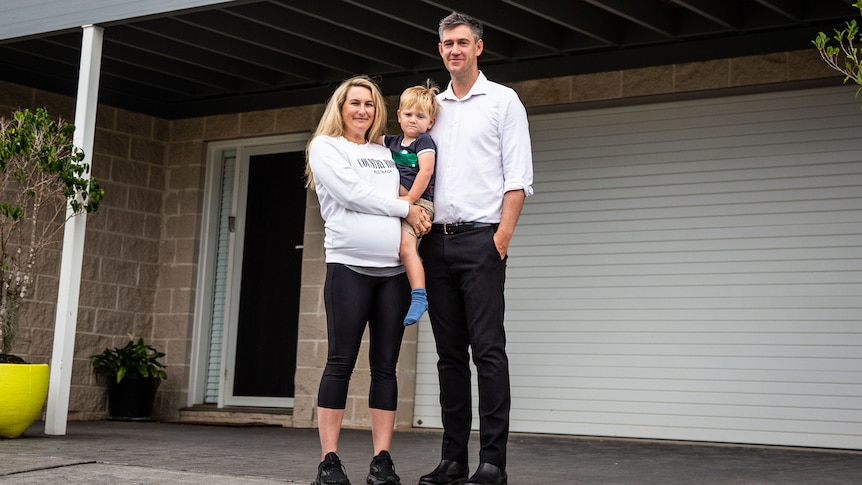 Fiona Fagan and Richard Sykes stand in front of their garage, Fiona is holding their son.