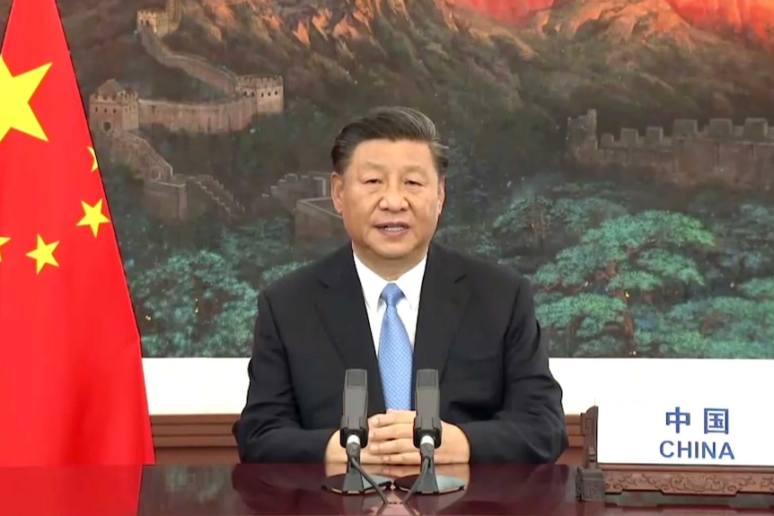 Xi Jinping sitting staring straight at a camera with a Chinese flag and a mountainous backdrop featuring the Great Wall of China