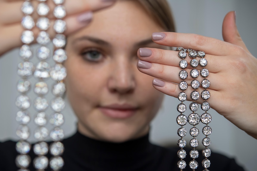 A woman holds up diamond bracelets in each hand. 