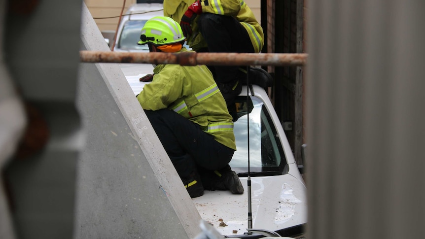 Firemen work on a crushed car under a large concrete block.