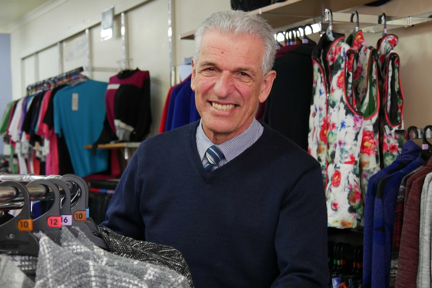A man stands in a women's clothing store, among racks of clothes.