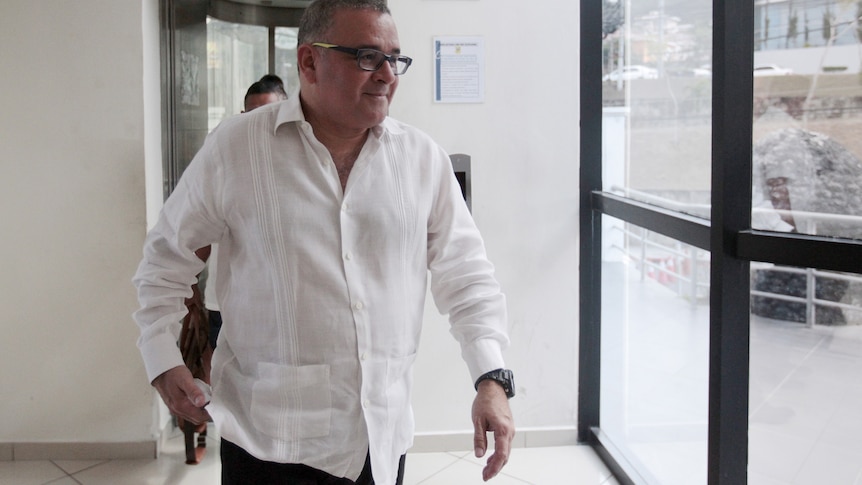 Maurcio Funes walking wearing a white button up shirt and glasses.