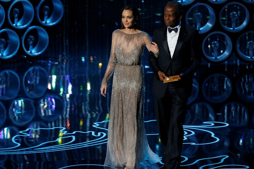 Actors Angelina Jolie and Sidney Poitier walk together on stage.