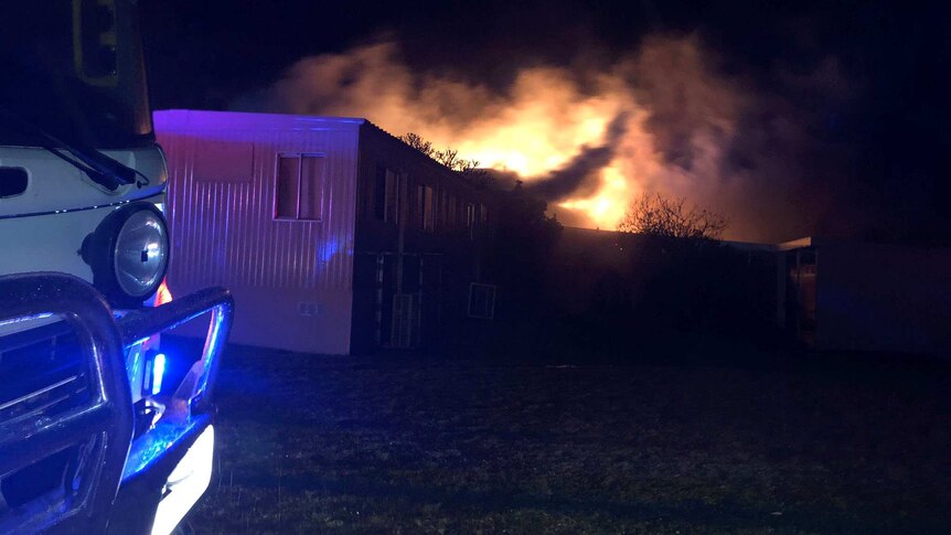 A fire blazes against a night sky with a demountable building and truck in the foreground.