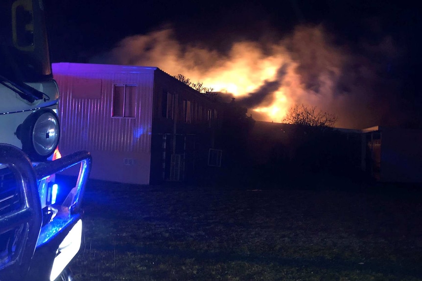 A fire blazes against a night sky with a demountable building and truck in the foreground.