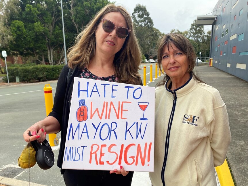 Adelia Berridge with a protestor holding a sign that says: sorry to wine, mayor KW must resign.