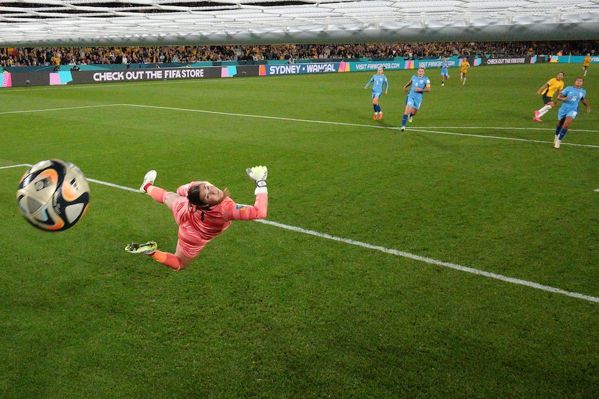 A goalkeeper wearing all pink looks over her shoulder at a ball that flies past her during a game