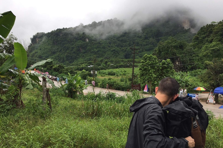 Marsic filming people walking along road next to green mountain shrouded in mist.