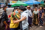 A young woman holding flowers cries as another woman comforts her and others look on.
