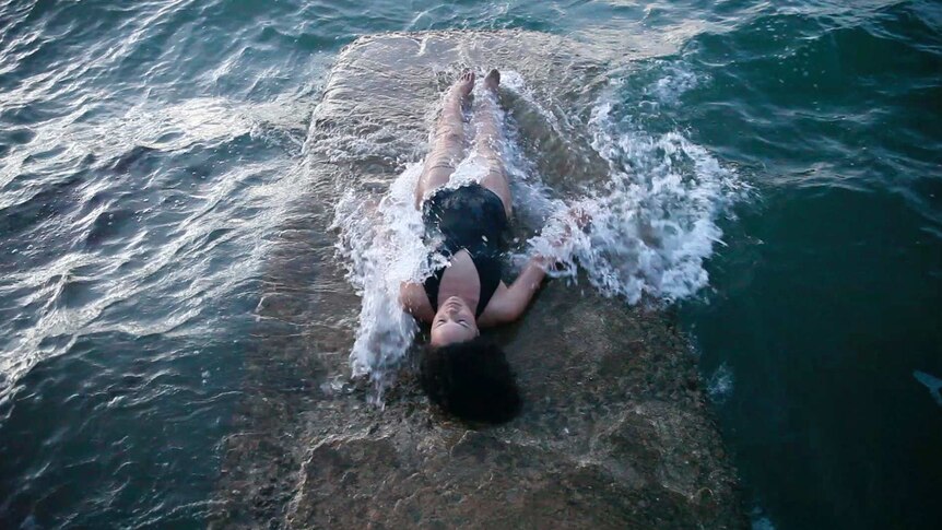 A woman in bathers lying on a slab of stone on the surface of the ocean