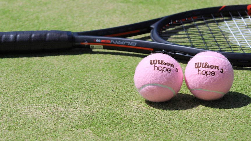 Two tennis racquets on a tennis court with two pink tennis balls
