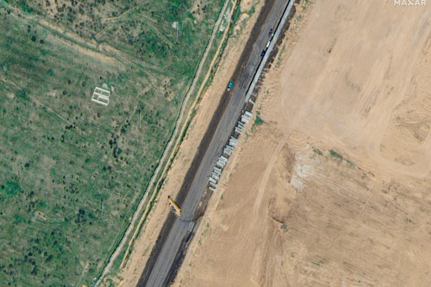 A satellite image of a road with onstruction and trucks lining one side 
