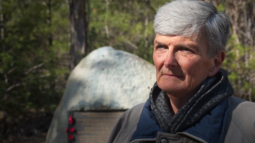 A mature aged author with grey hair stands at the memorial site.