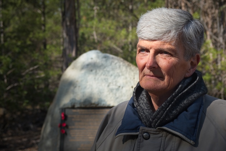 A mature aged author with grey hair stands at the memorial site.