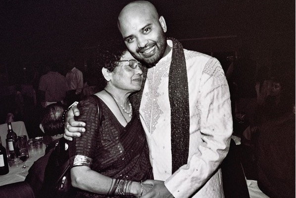 An older woman wearing a sari embraces her son at his wedding. 