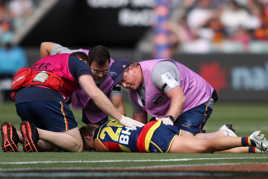 An Adelaide Crows AFLW player lies on the ground being attended to by medical staff after sustaining a concussion.