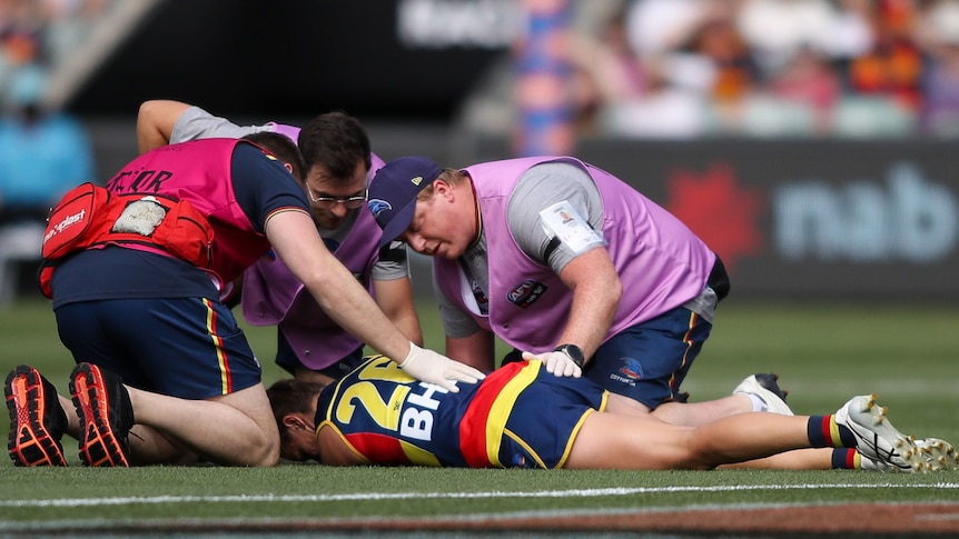 An Adelaide Crows AFLW player lies on the ground and is attended to by medical staff after being concussed.