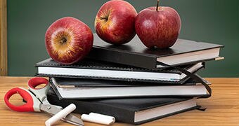 Apples and scissors on some notebooks on a desk.