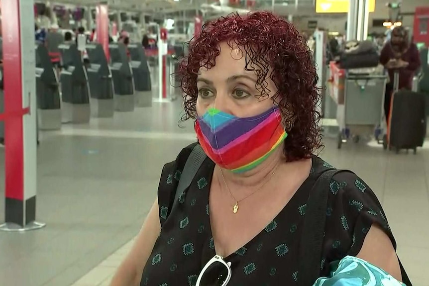 A woman wearing a masks stands in the airport domestic terminal.