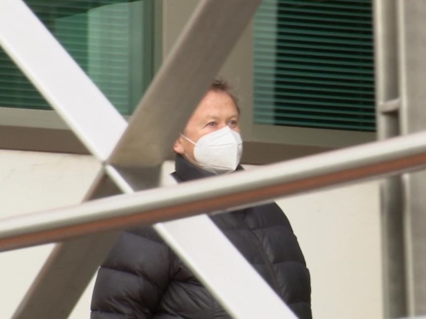 A woman wearing a black puffer jacket and face mask seen through metal bars.