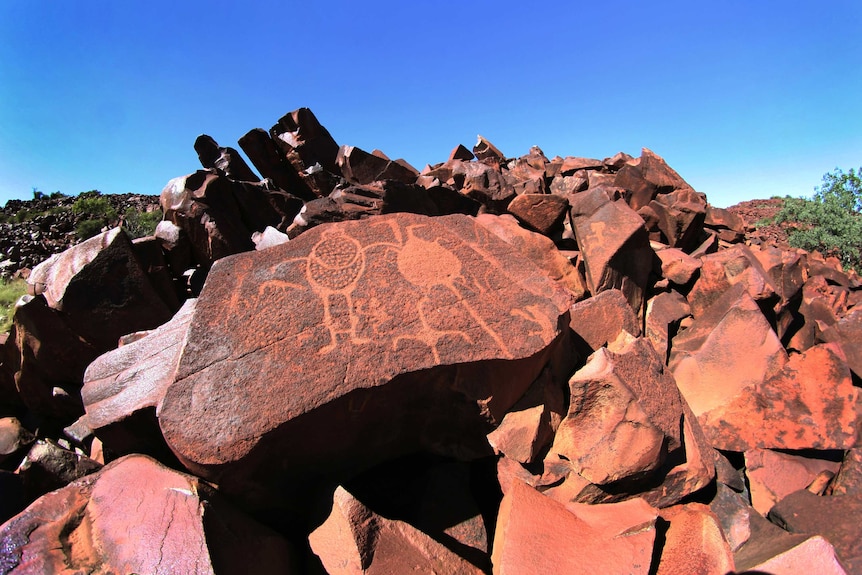 A pile of red rocks with figures carved into them and a blue sky behind