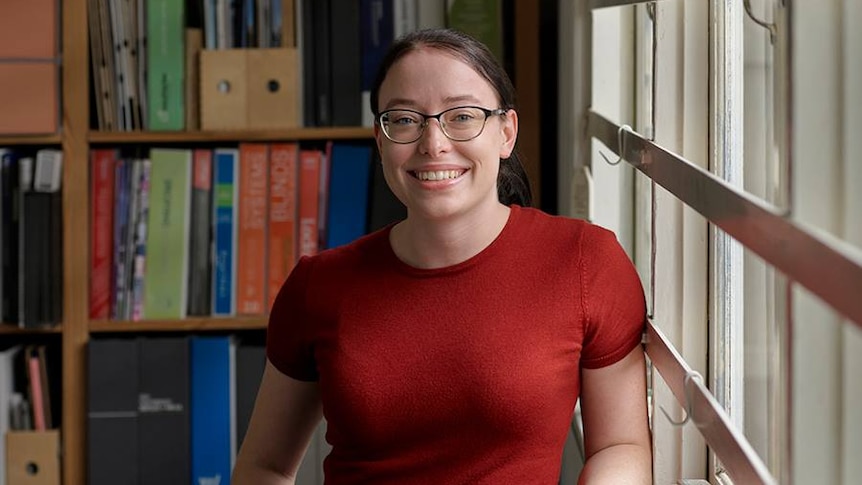 An image of a young woman standing in front of a book shelf