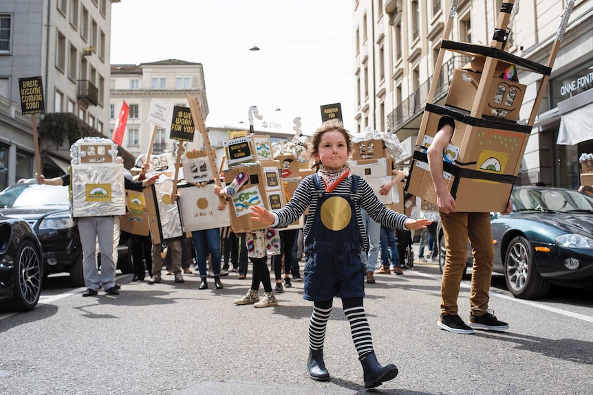 A child leads a parade of basic income activists dressed as robots in Zurich, Switzerland.