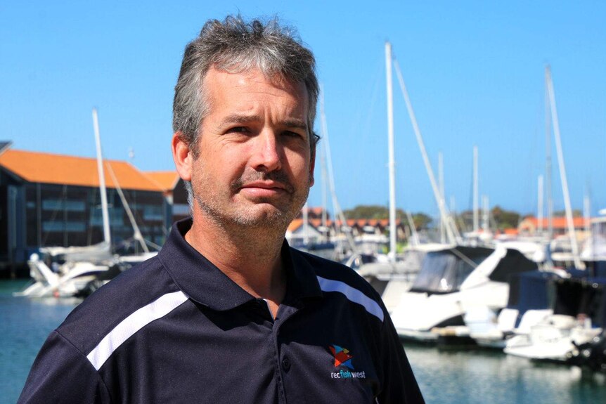 Leyland Campbell standing near the water at a boat harbour with yachts in the background.