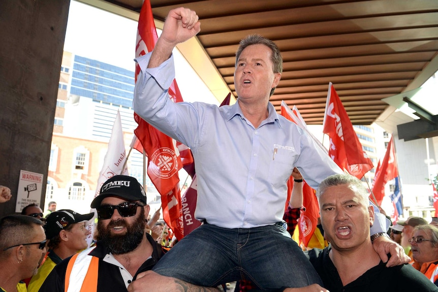 A man at the centre of a flag waving crowd sits on people's shoulders cheering