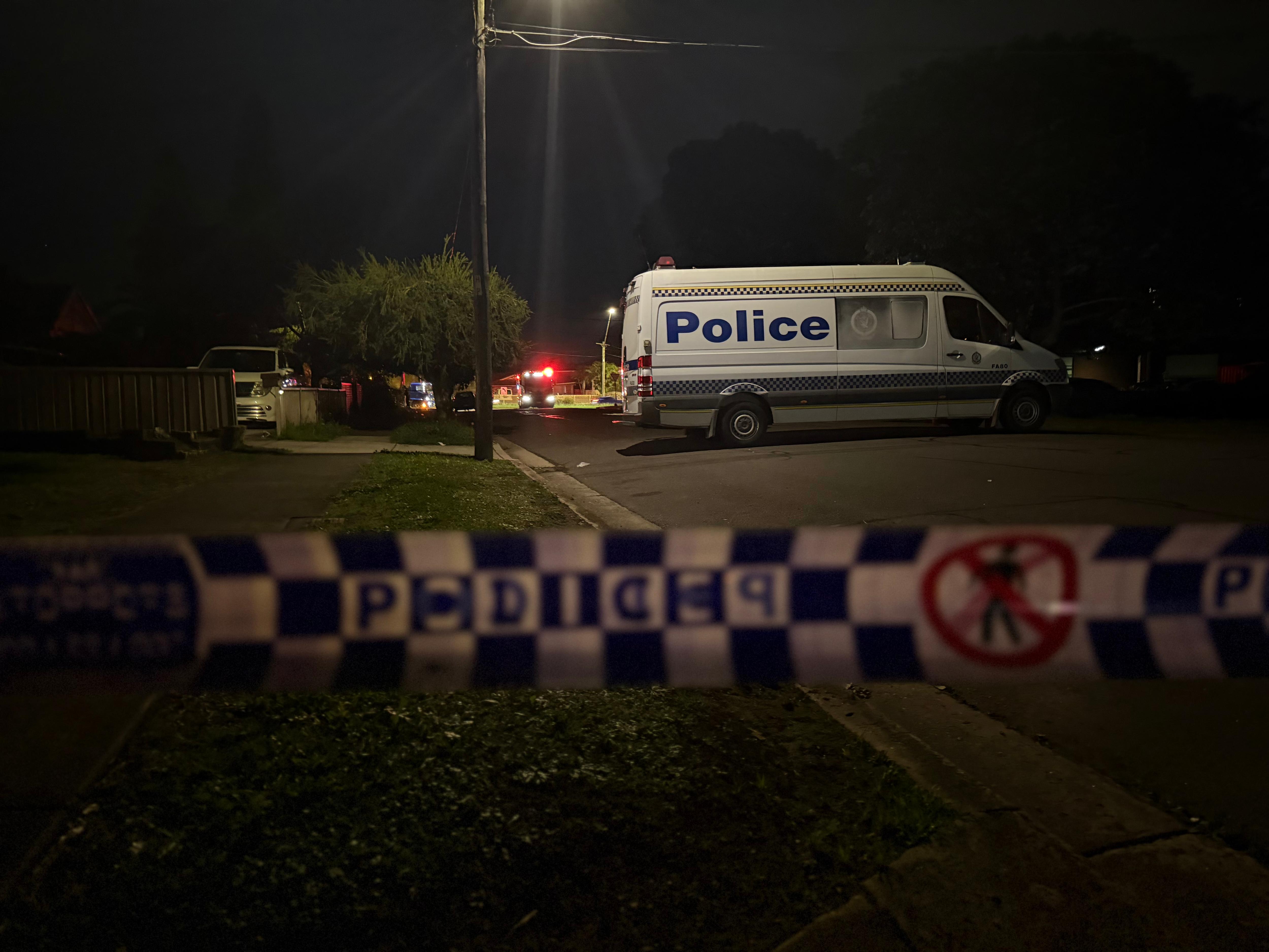 A dark night scene with police tape at the front and a police car in the back.