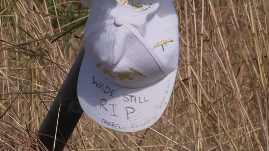 a white hat cap on a pole in front of brown grass. It reads Wade Still RIP.