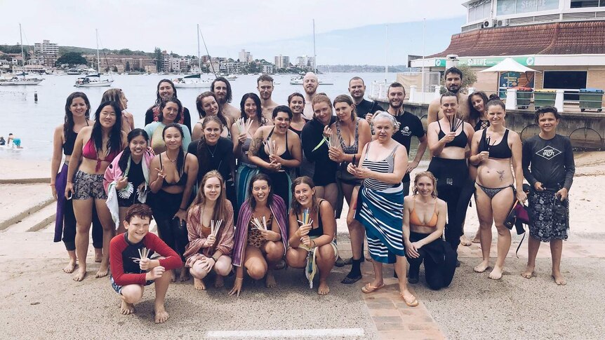 A group of people holding plastic straws recovered at Manly Cove.