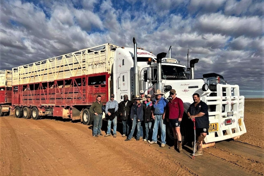 Cattle station staff stand in front of a truck full of cattle in dry red dirt 